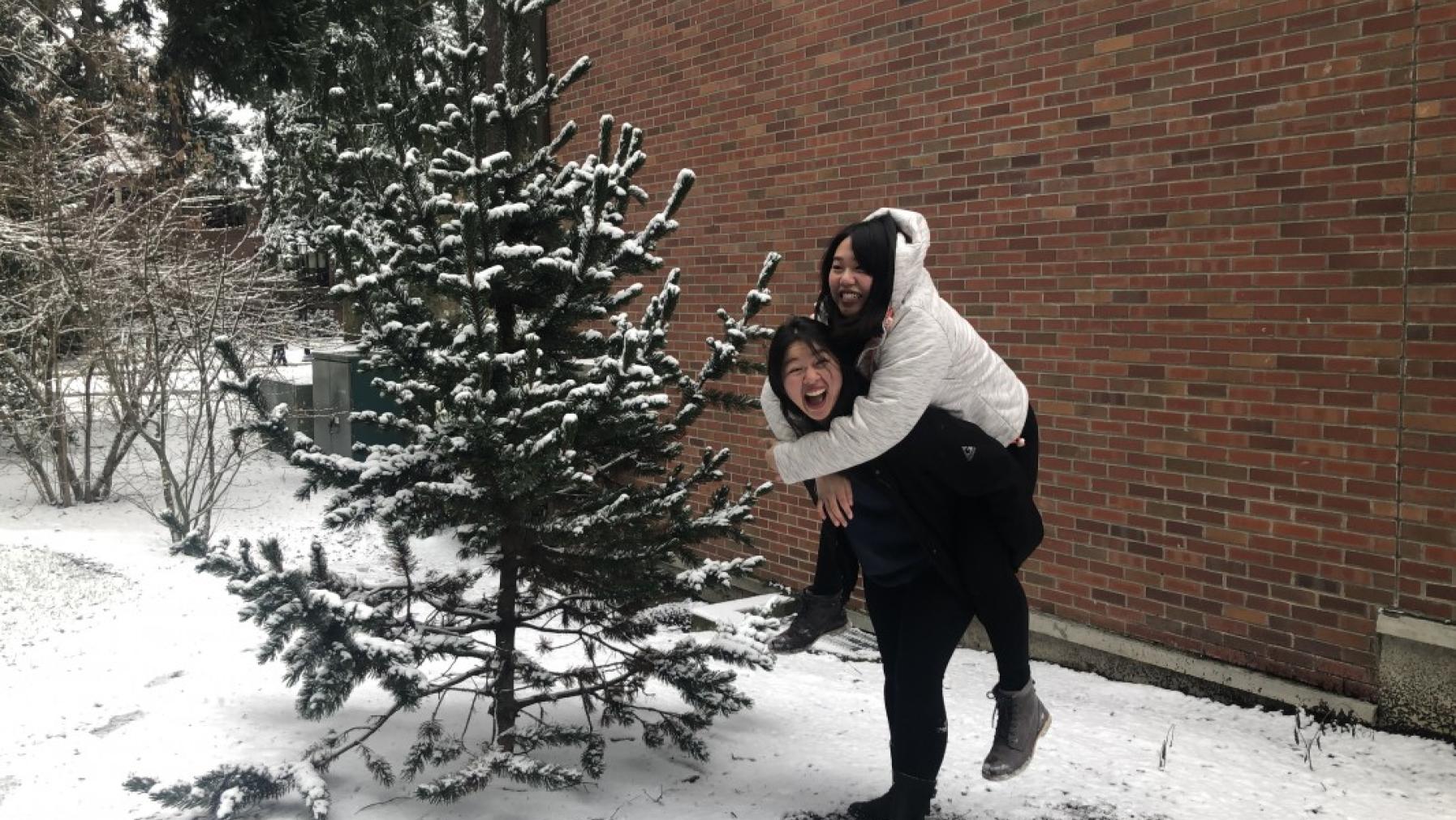 Two people in the snow in front of a tree.