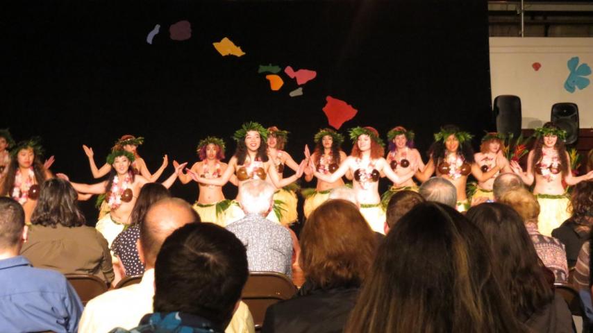 A group of people wearing hula skirts dancing.