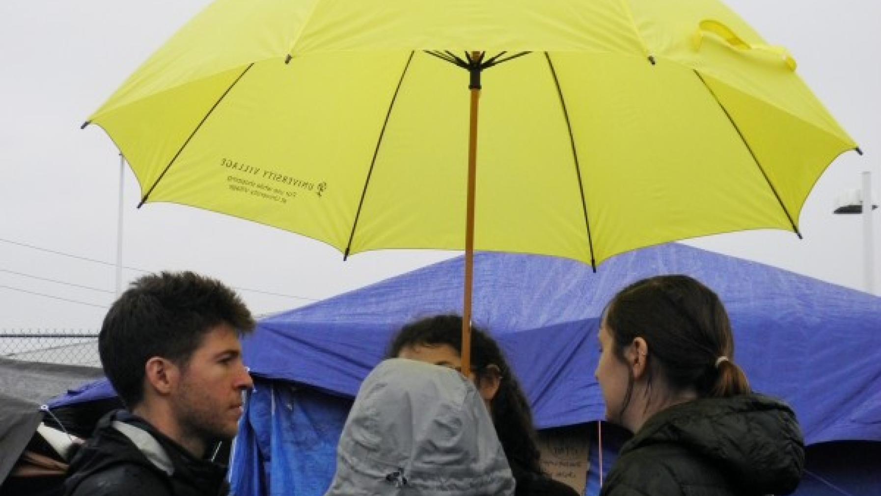 Four people standing under an umbrella.