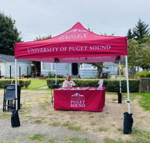 A Puget Sound staff member represents the university at a local community events with a branded pop-up tent and fitted tablecloth.