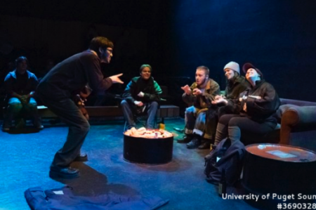 Actors gathered around a campfire on stage