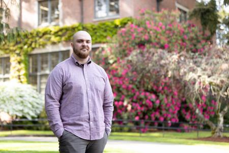 Nathan Durham stands in front a rose bush on campus. 