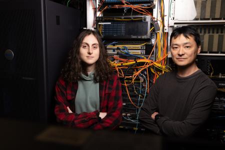 Julia Keppel stands next to Prof. David Chiu in front of stacked computers with wiring sticking out. 