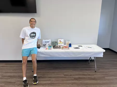 Tdohasan sits on a table with books from the camp displayed.