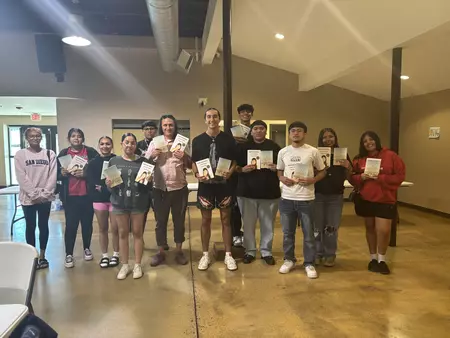 Students line up holding a book