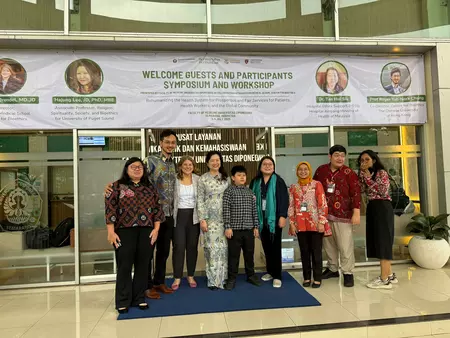 Prof. Hajung in a group photos with a banner above her.