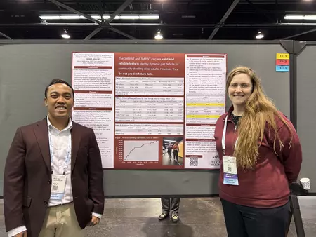 Two students pose in front a research poster. 