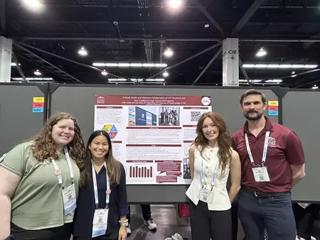 Four students pose in front of a research poster.