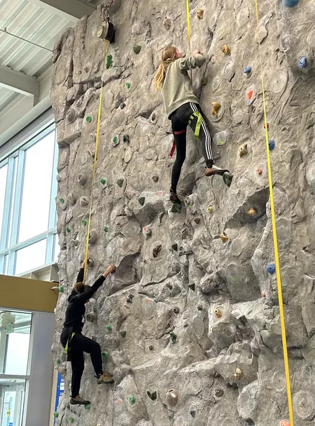 Two students climb a rock wall. 