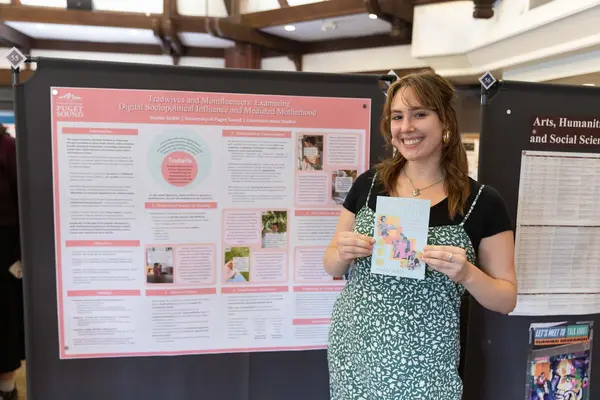 Sophie Goble poses with her zine in front of her research poster. 