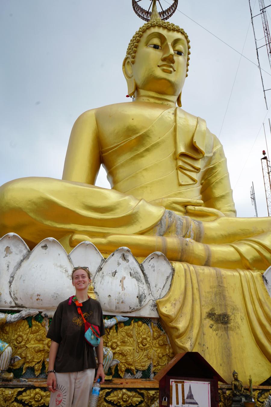 Rhae Schulz-O'Neil standing infront of a large golden Buddha in Thailand